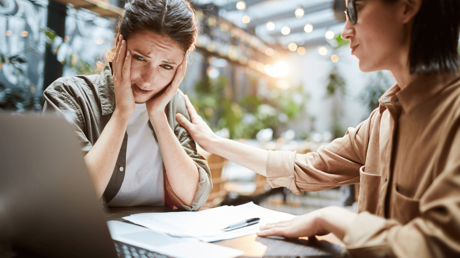 Duas mulheres conversando em uma mesa de trabalho, enquanto uma delas demonstra preocupação diante do computador e a outra oferece apoio, representando desafios, tomada de decisão e orientação profissional.