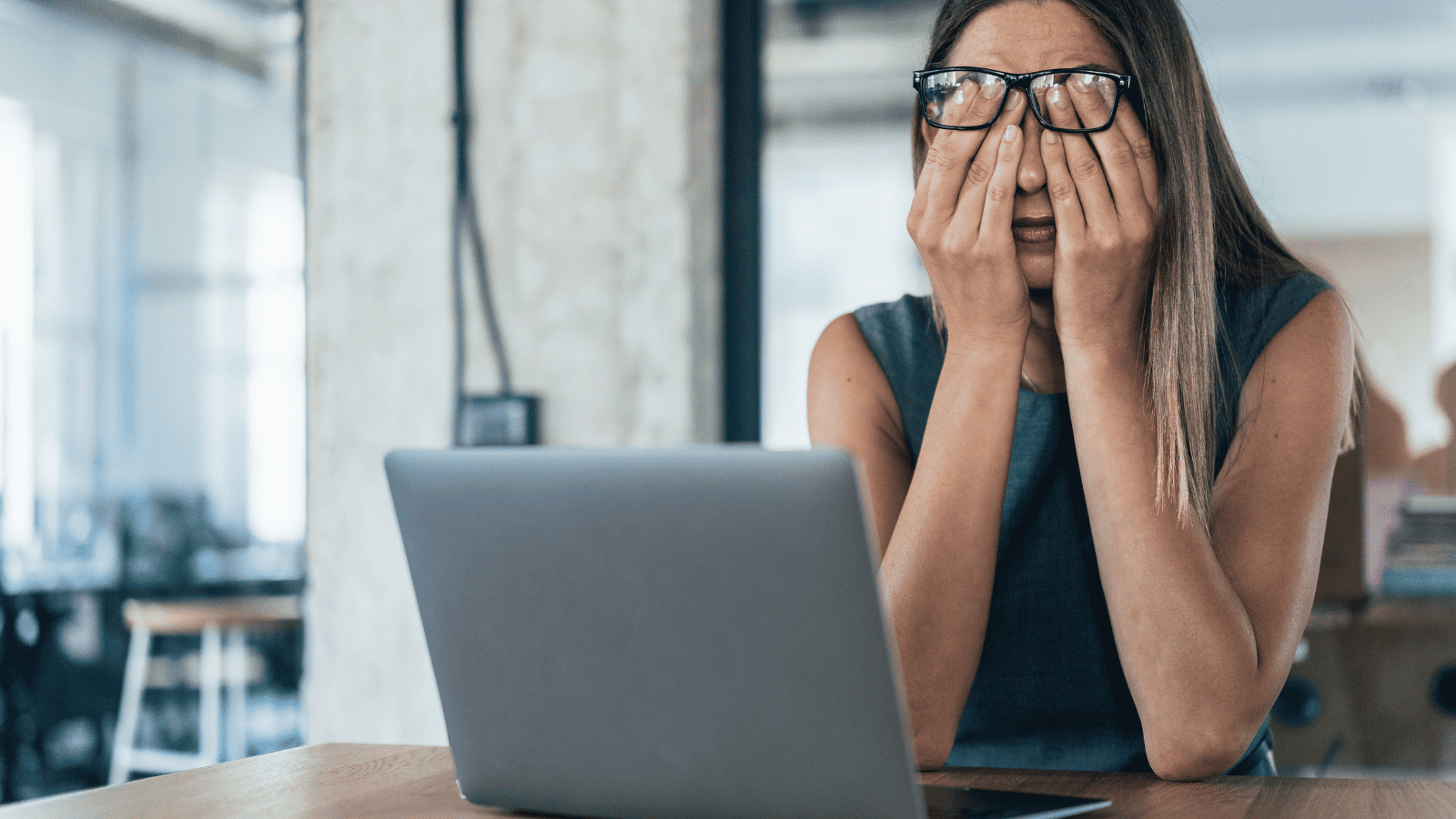 Mulher demonstrando cansaço e preocupação diante de um notebook em ambiente de trabalho, representando sobrecarga, estresse profissional e desafios na gestão do negócio.